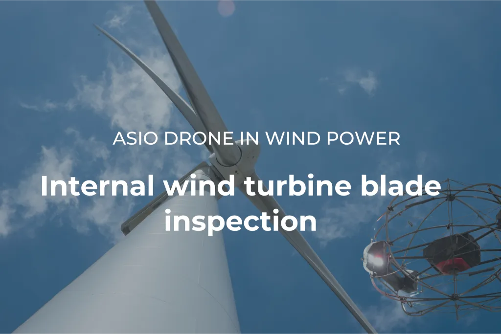 ASIO X drone next to a wind turbine tower, photographed from below against a blue sky. Internal blade inspection proof of concept.